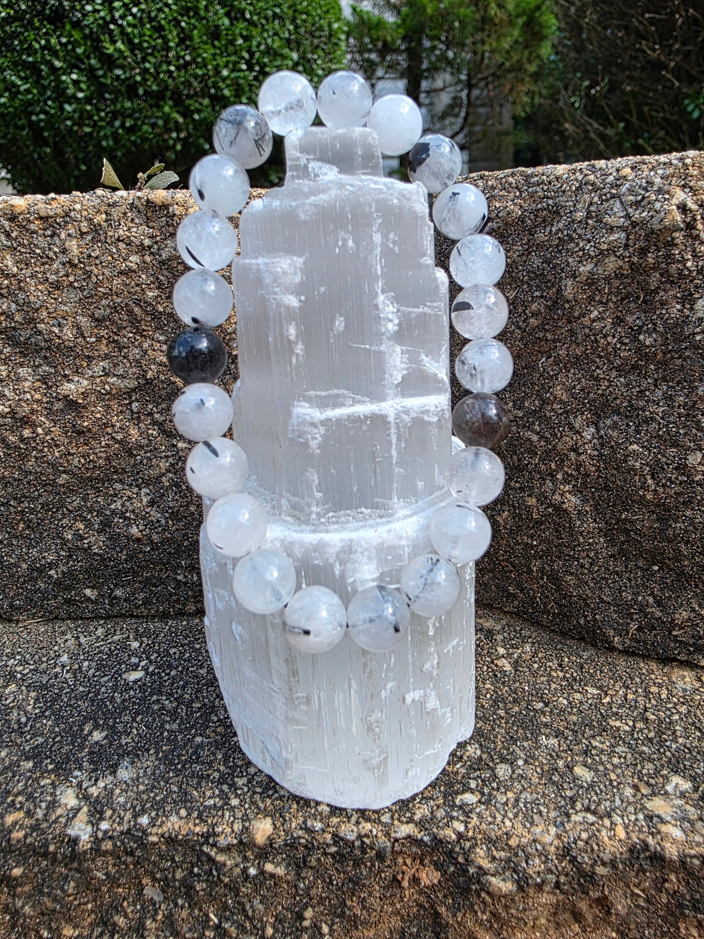 Rutilated quartz bracelet featuring clear beads with black rutile needles, displayed on a selenite tower; this gemstone is believed to amplify clarity and energy.