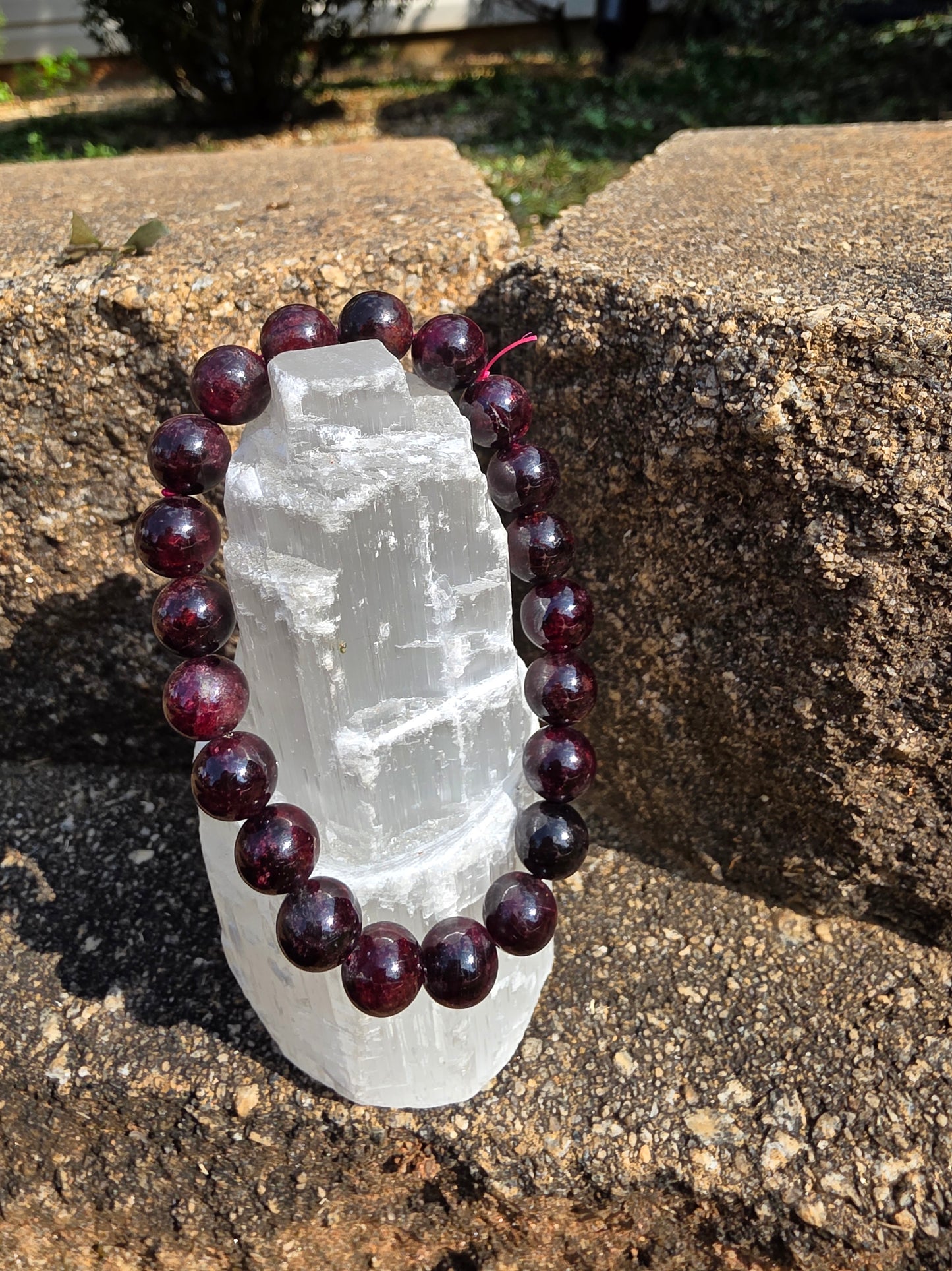 Starlight Garnet bracelet featuring round 10mm deep red garnet beads wrapped around a selenite tower on a stone surface; this stone inspires passion, courage, and grounding energy.