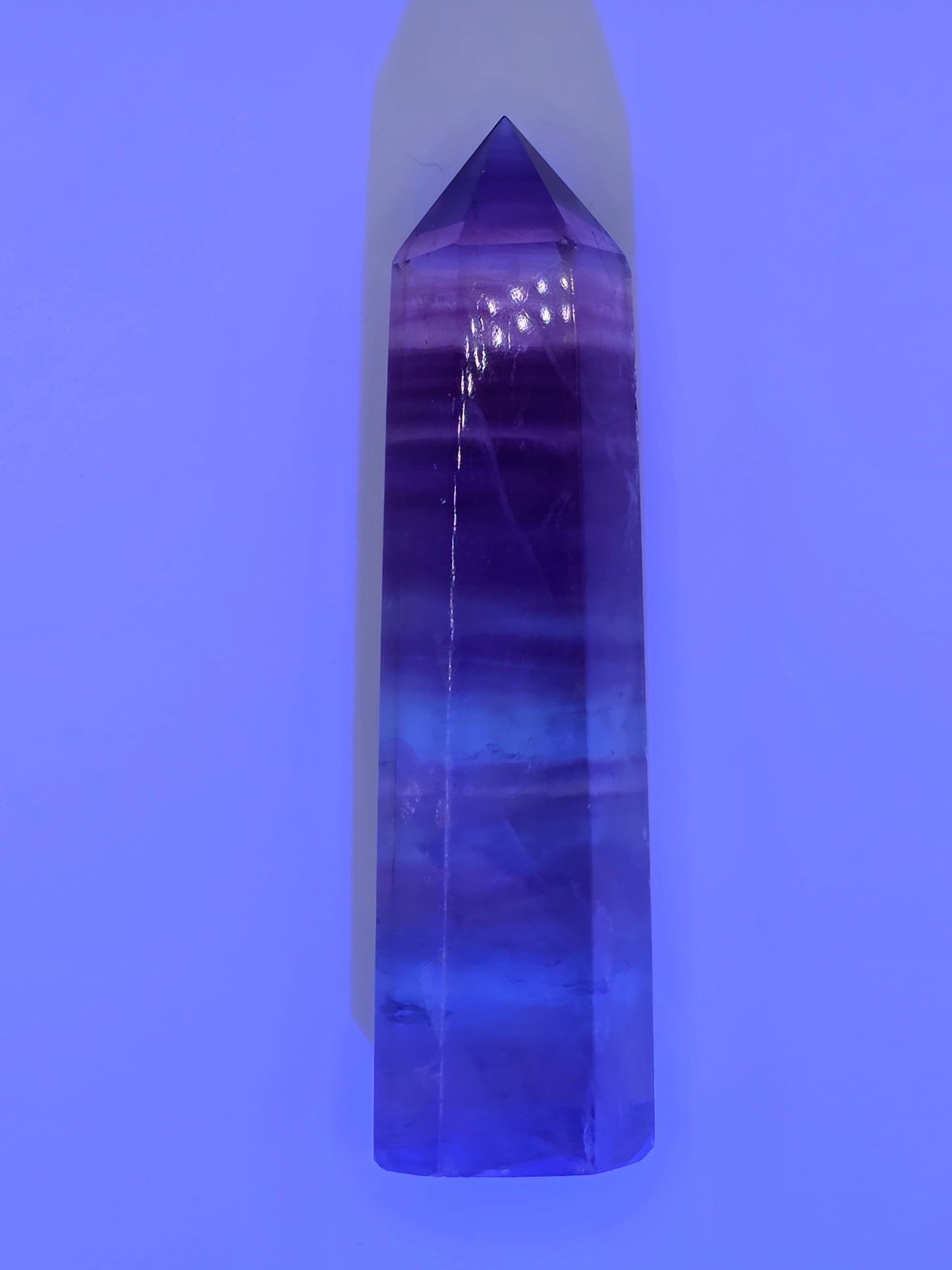 Fluorite tower glowing under UV light with rich purple luminescence.