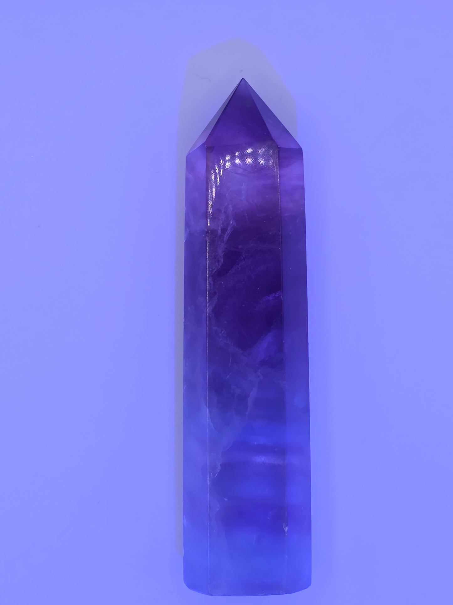 Fluorite tower glowing under UV light with vibrant violet hue.
