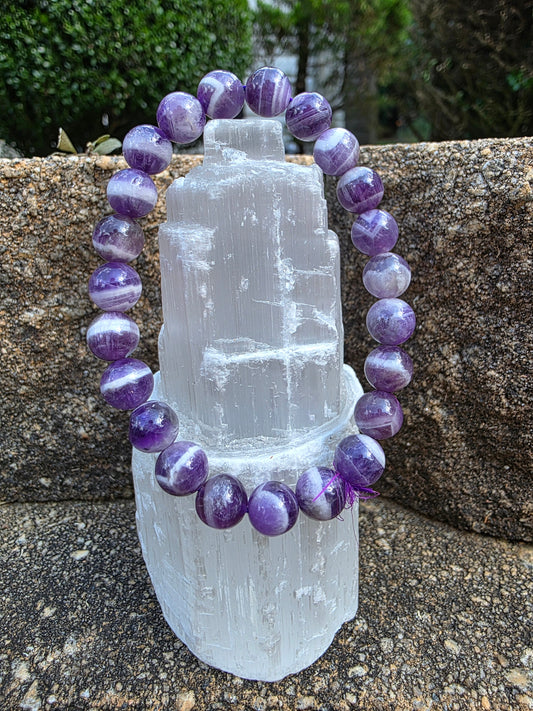 Dream Amethyst bracelet featuring 8mm beads with swirling purple and white bands, displayed on a selenite tower; this chevron amethyst supports intuition and calm.