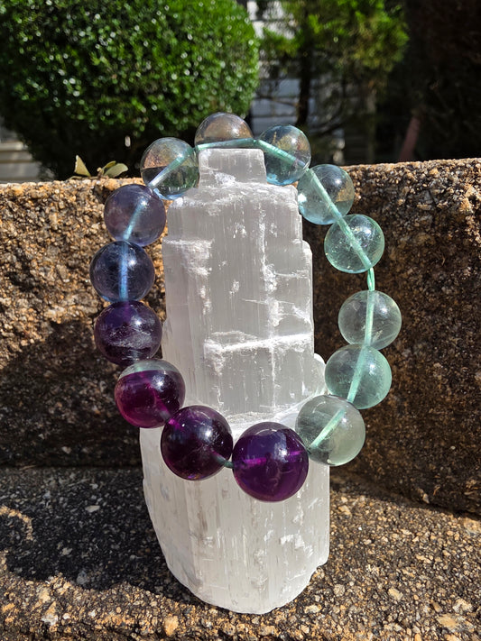 Fluorite bracelet featuring round 8 mm beads in translucent green, teal, and purple hues, draped around a selenite tower; a stone of focus, protection, and spiritual clarity.
