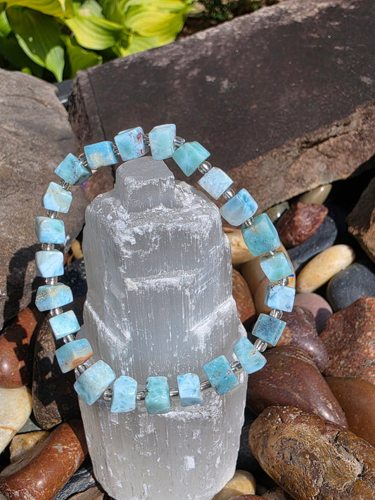 Larimar bracelet featuring Caribbean blue beads with white and turquoise swirls, displayed on a selenite tower; a soothing stone for communication and calm.