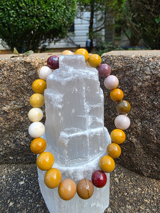 Mookaite bracelet featuring 8mm beads in warm earth tones of mustard, cream and red, displayed on a stone surface; encourages adventure and grounded decision-making.