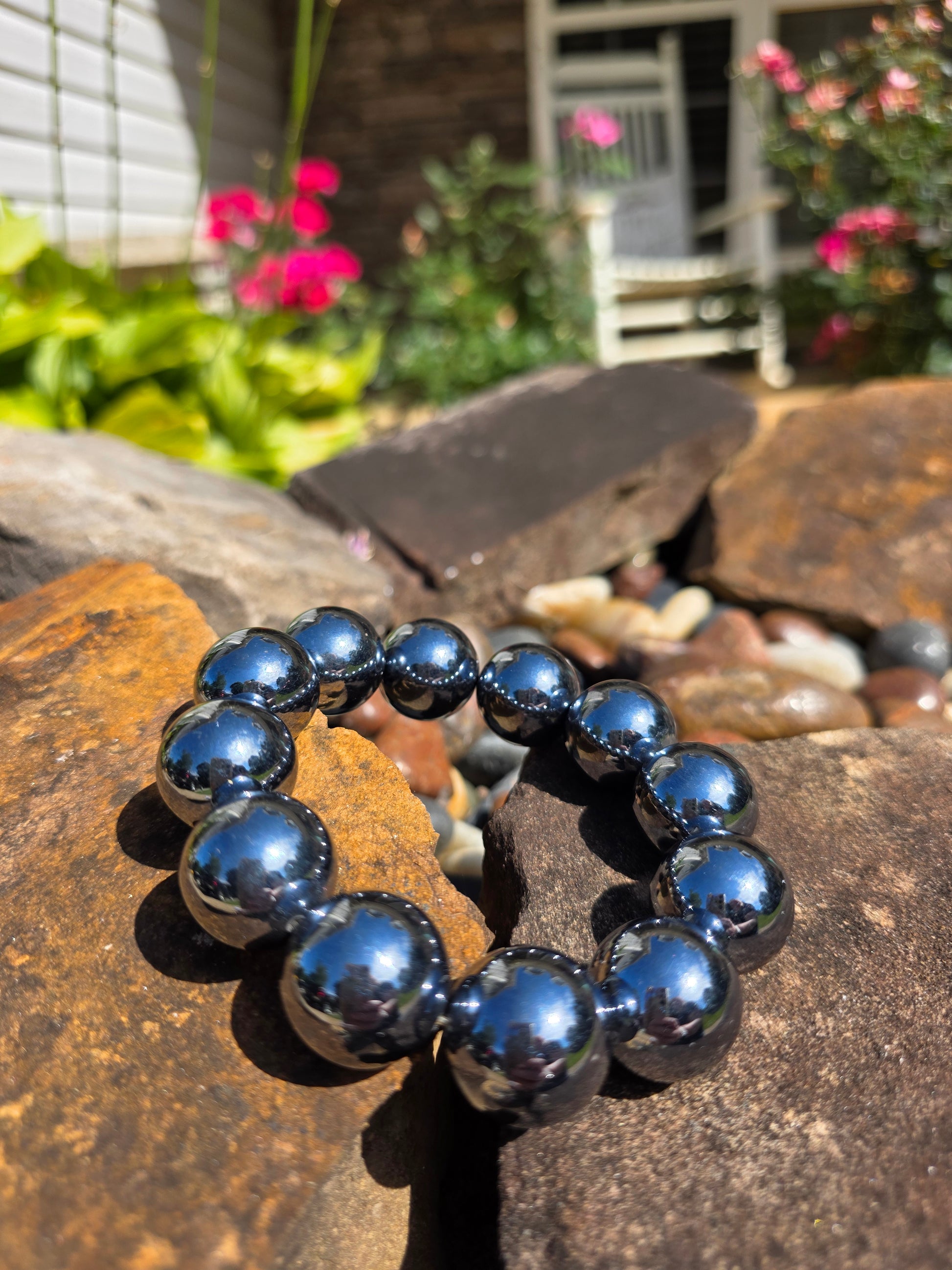 Terahertz bracelet featuring large 12mm metallic grey beads with high shine, displayed on a stone surface with a garden background, known for high-frequency energy and stress relief