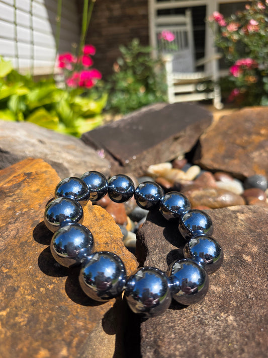 Terahertz bracelet featuring large 12mm metallic grey beads with high shine, displayed on a stone surface with a garden background, known for high-frequency energy and stress relief