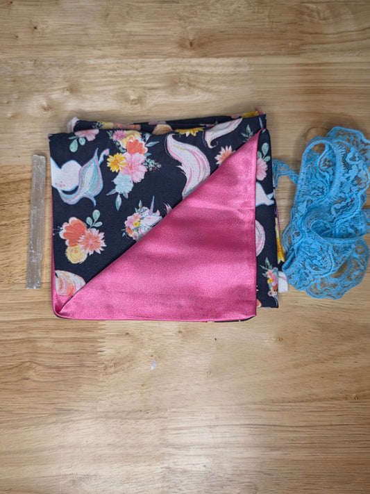 Handmade tarot wrap featuring navy fabric with pastel unicorns and floral designs, pink satin lining, turquoise lace tie, and selenite stick for cleansing and protection.