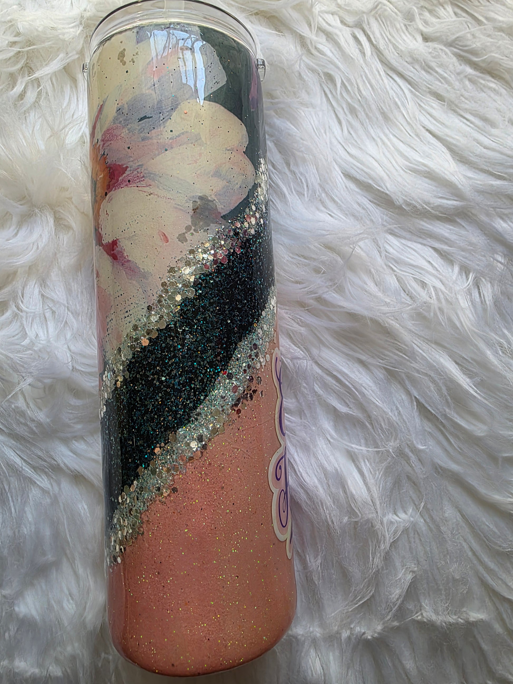 Epoxy tumbler showing the phrase The Earth Laughs in Flowers in purple script on a glittery peach and teal background