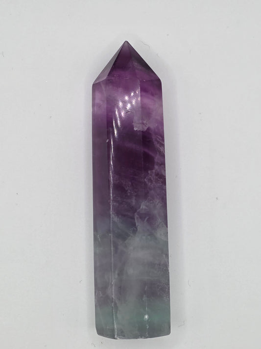Fluorite tower with purple-to-green banding, polished surface on light background.
