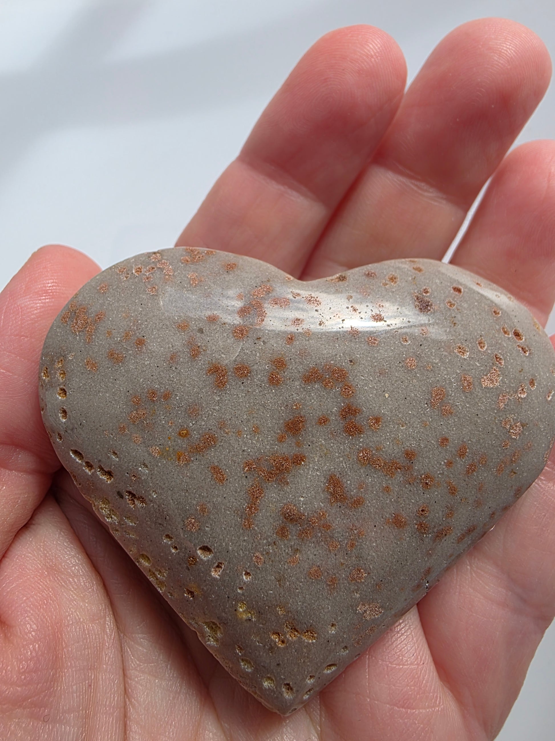 Close-up of a Sunstone heart held in hand, showing copper shimmer and soft tan tones with natural sparkle under sunlight.