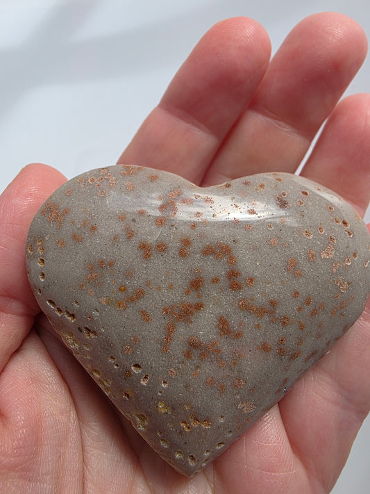Close-up of a Sunstone heart held in hand, showing copper shimmer and soft tan tones with natural sparkle under sunlight.