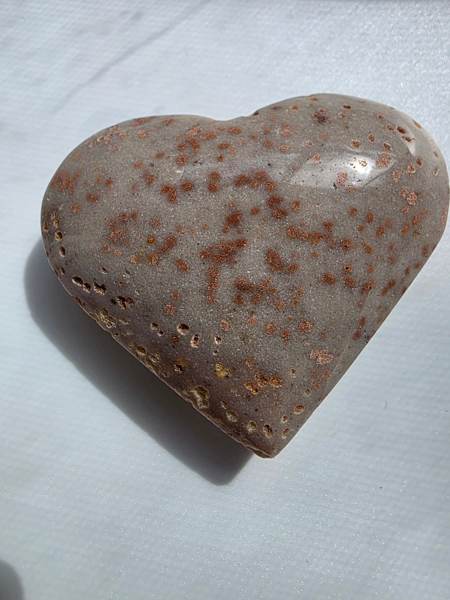 Sunstone heart carving lying flat in sunlight, highlighting peach and copper shimmer across a warm beige surface.