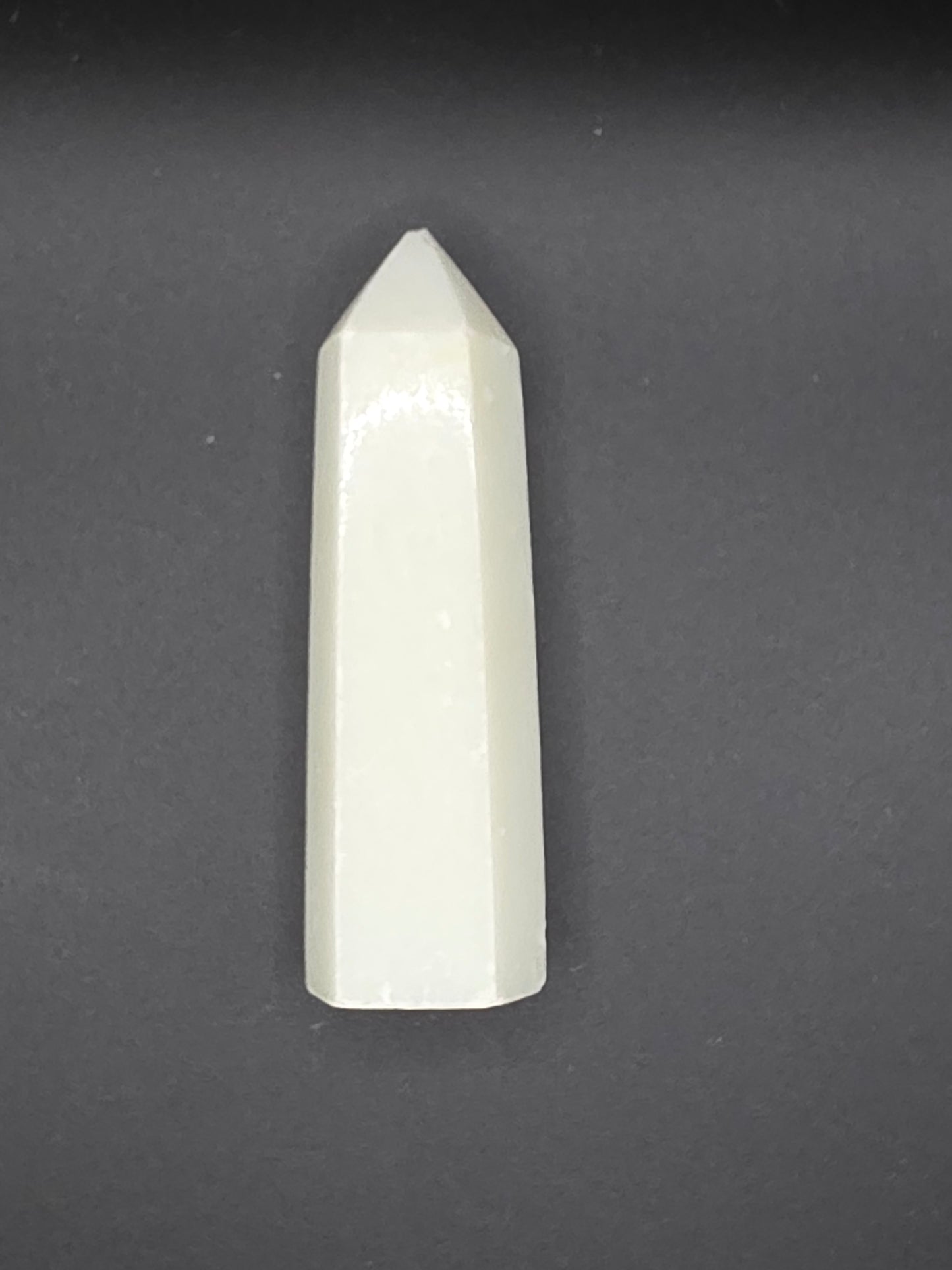 White Calcite tower with creamy translucence and slightly chipped tip on a black background.