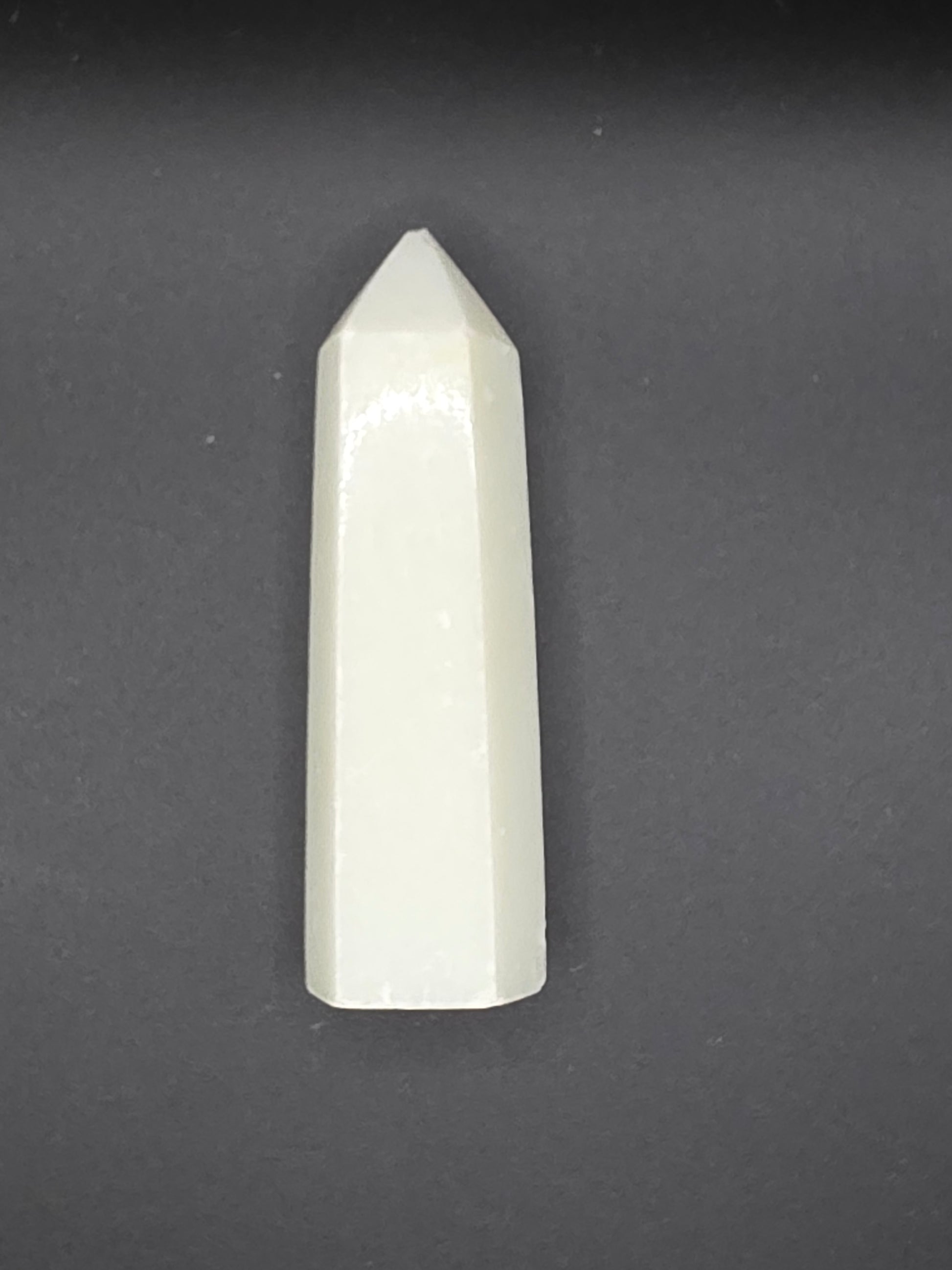 White Calcite tower with creamy translucence and slightly chipped tip on a black background.