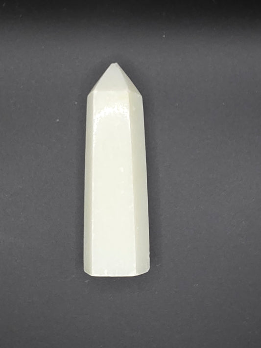 White Calcite tower with creamy translucence and slightly chipped tip on a black background.